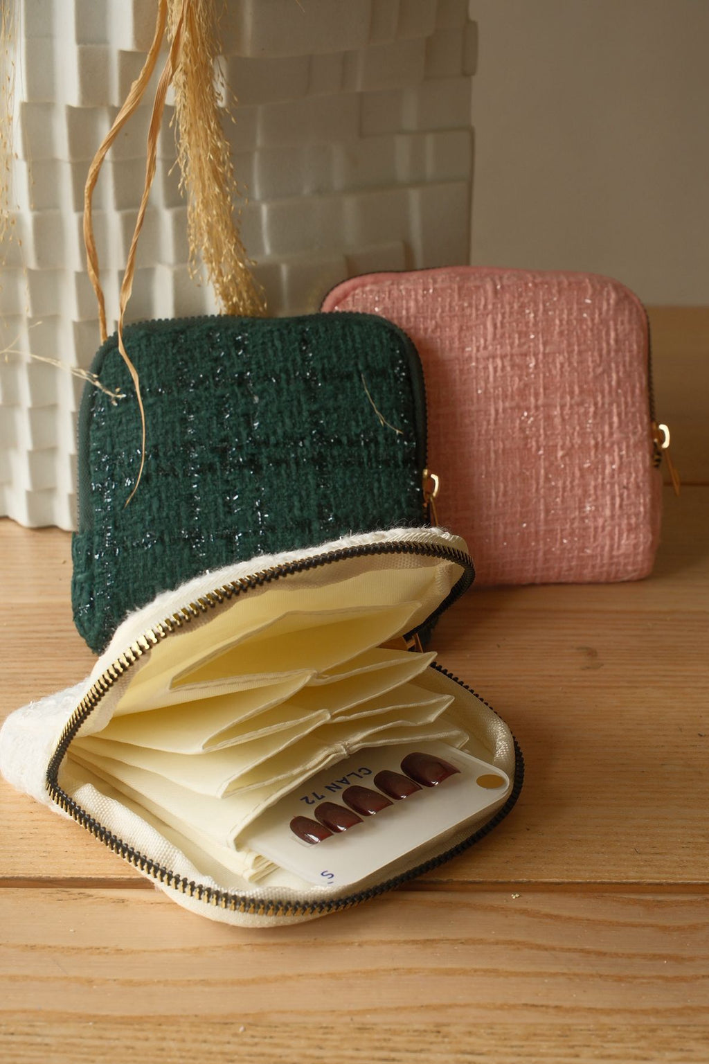 Two small bags, one green and one pink, on a wooden surface with an open beige pouch containing small items.