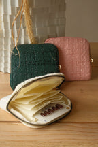 Two small bags, one green and one pink, on a wooden surface with an open beige pouch containing small items.